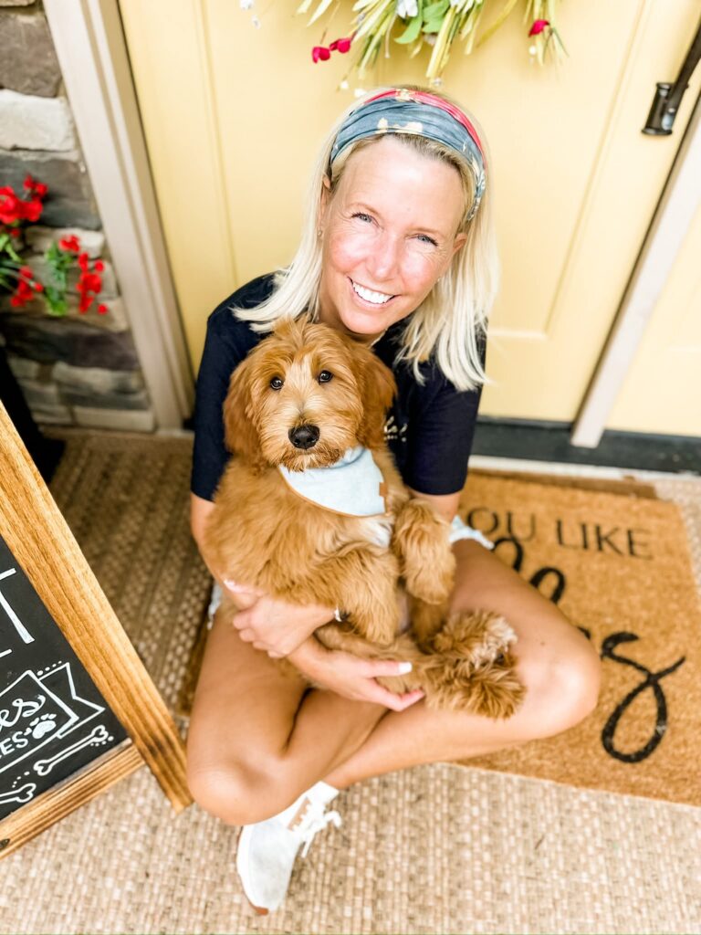 Smiling woman hugging a red multigen Goldendoodle puppy from BellaDoodles on a front porch